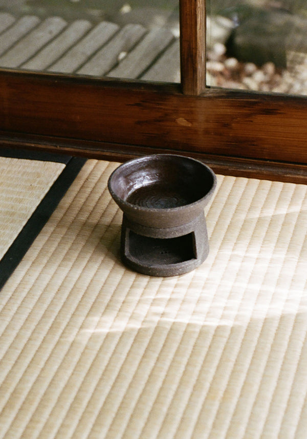 Ceramic Oil Burner | soil: A rustic, handmade oil burner on a tatami mat, designed by Alex Gabriels, featuring a bowl for oils and a base for tealight heating.