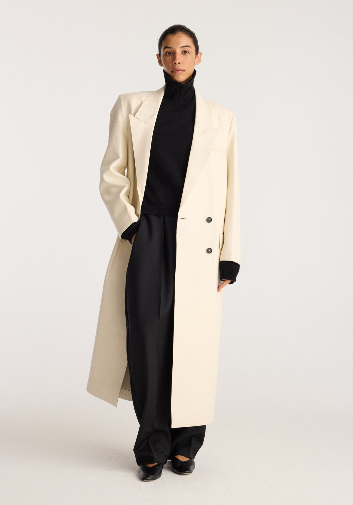 Menswear Inspired Bonded Leather Coat | chalk modeled by a woman over a black turtleneck and wide leg trousers in a minimalist studio setting