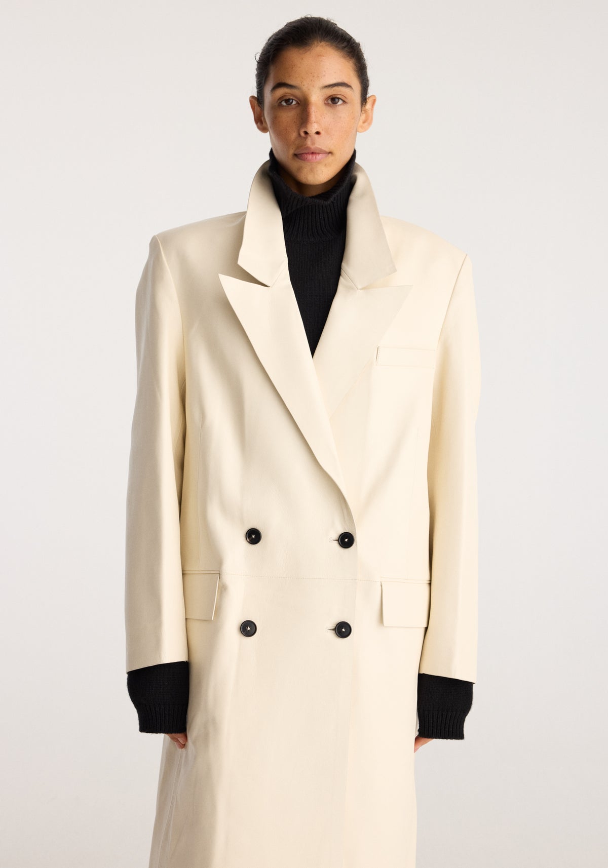 Menswear Inspired Bonded Leather Coat | chalk shown on a model with a cream double breasted design and wide lapels over a black turtleneck sweater